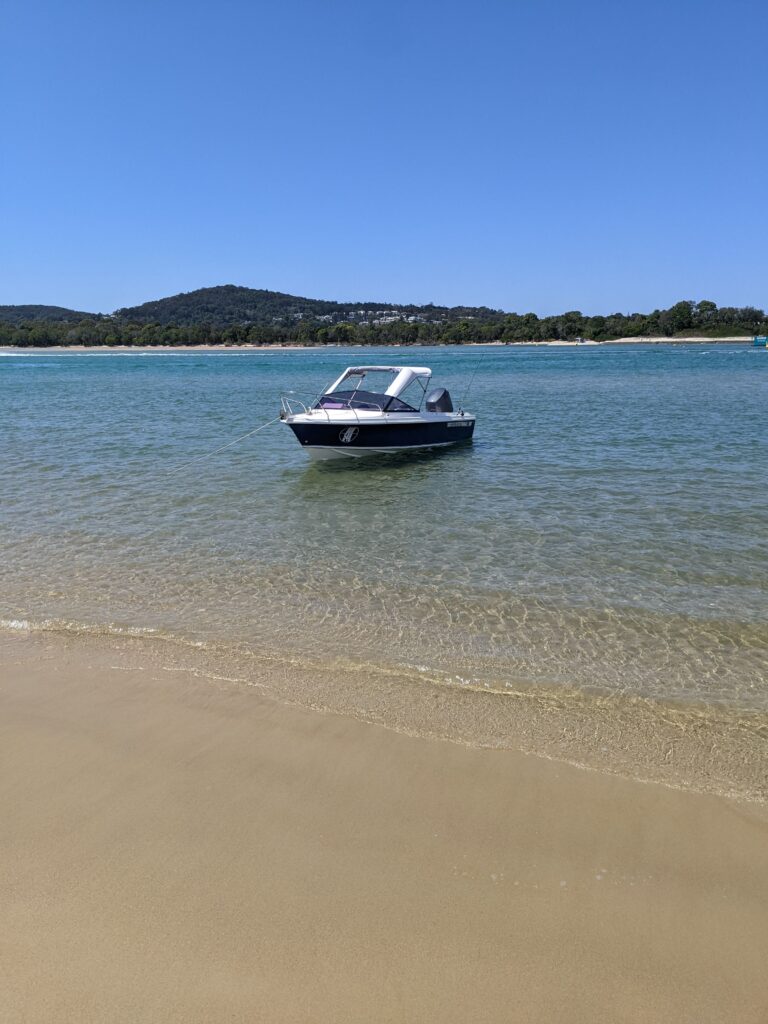 A Boat Peacefully Floats on The Water Near a Sandy Beach — Secondhand Boat Motors in Hervey Bay